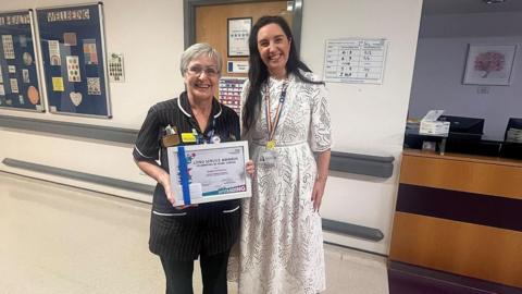 Angie holding her achievement certificate alongside her colleague 
