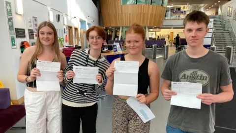 Students Megan Green, Noctis Clark, Molly Moore and Toby Groom stand in  a line, each holding their results in front of them