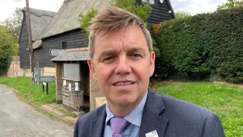 Ben Schofield/BBC Nik Johnson standing outside wearing a blue suit