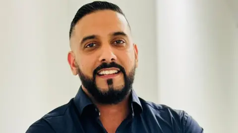 Young man with a beard, moustache and wearing an open-necked blue shirt