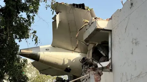 A tail of an Air India Boeing 787 Dreamliner plane that crashed is seen coming out of a building