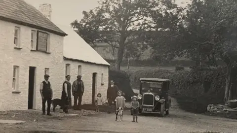 Under the Thatch A black and white photo showing a small group of people and a now vintage car outside the pub