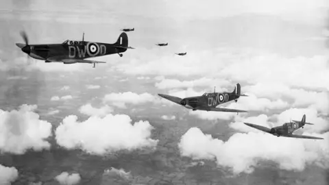 Three spitfires flying above the clouds. black and white image. It also shows three more spitfires in the background and fields can be seen below them