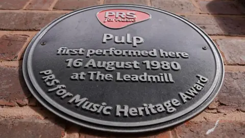 Getty Images A black circular plaque attached to a bricked wall. The plaque reads: 'Pulp first performed here 16 August 1980 at The Leadmill. PRS for Music Heritage Award.'