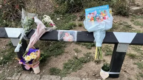 Richard Knights/BBC Flowers left by a fence on a street where Gary Hindle was killed. They are taped to a wooden fence. There is a picture of Gary also taped to the fence.