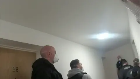 Police officers can be seen in a hallway, two of whom are wearing masks