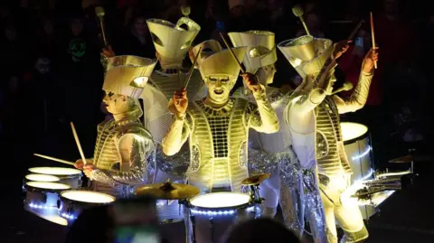 PA Media Five performers, dressed in elaborate white costumes, pictured playing drums during the Derry Halloween parade in Londonderry in 2022