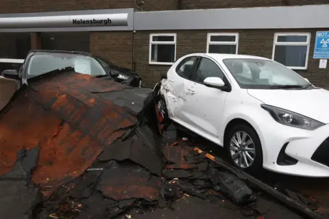 Getty Images Debris that looks like it has been blown from a roof strewn on top of a black car. A white car sitting next to it has also been damaged