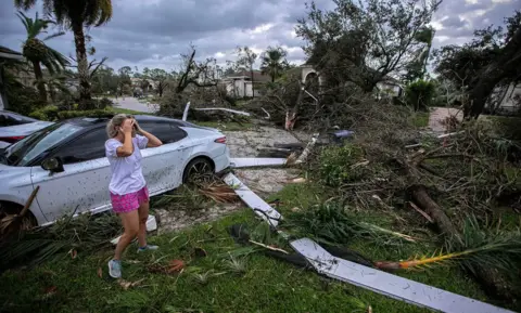 Bill Ingram / Palm Beach Post Marie Cook holds her head and reacts to the damage to her home in the Binks Estates community, with a car and felled trees in shot, in Wellington, Florida, U.S. October 9, 2024