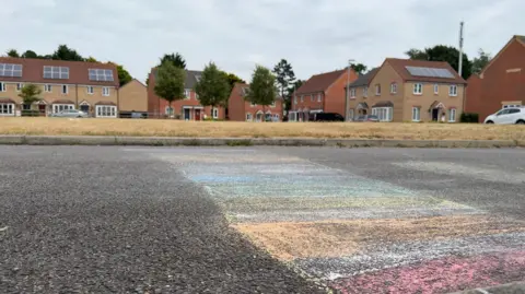 Colourful chalk markings are drawn onto the road between a path and grassy area at the centre of the housing estate
