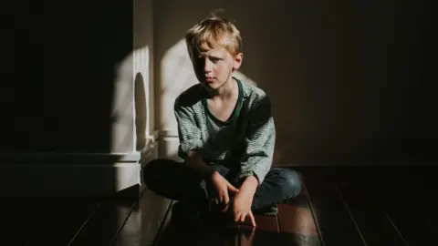 Getty Images A young boy sat alone on a wooden floor, staring sadly at the camera