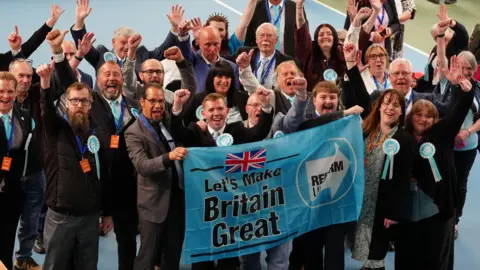 PA Media A group of Reform UK members at the election count in Sunderland. They are cheering and holding a blue banner that reads, Let's Make Britain Great.