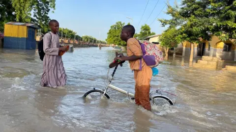     Ahmed Kingimi/Reuters Een jonge Nigeriaanse man waadt door diepe wateren veroorzaakt door zware overstromingen in Maiduguri, Nigeria - dinsdag 17 september 2024.