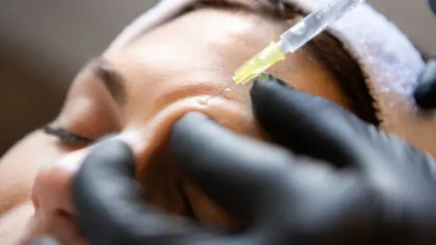Getty Images A close-up of a woman's face as she receives an injection just above her eyebrow. 