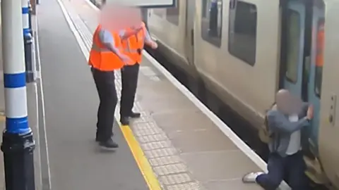 Railway staff assist a passenger who has fallen into the gap between a train and the platform.