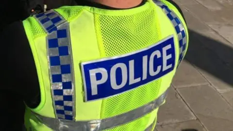 A police officer in a high vis tabard with the word POLICE in white