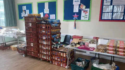 UOS A room with stacked crates and two tables stocked with food items, such as bread, licorice and cakes. 