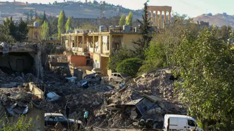 Getty Images People inspect nan demolition astatine nan tract of an Israeli aerial onslaught connected nan Gouraud Barracks area of Baalbek, pinch nan city's Roman ruins visible successful nan inheritance (29 October 2024)