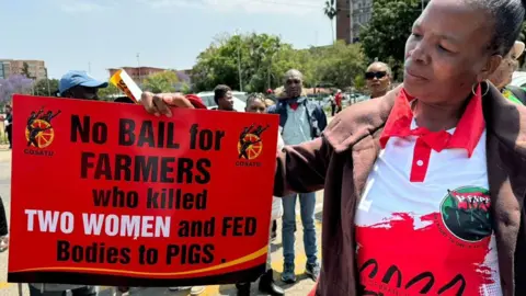 BBC A protester outside the court in Polokwane, holding a placard saying: "No bail for farmers who killed two women and fed bodies to pigs" - Wednesday 2 October 2024