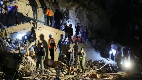 Getty Images First responders attend a damaged building at Los Palos Grandes at night. 