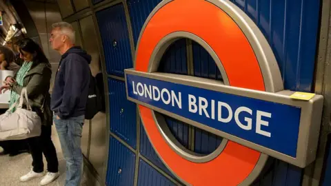 Getty Images A close up of a red Tube roundel with white letters on blue background, on a Tube station platform. It says London Bridge. 