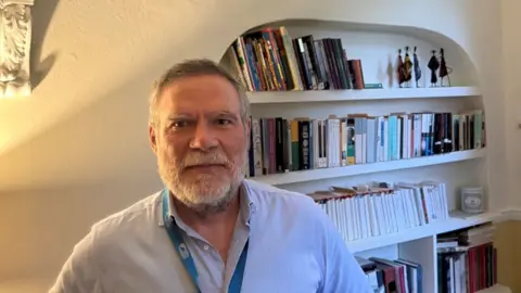 SUPPLIED Dr Neil Nixon standing in front of a bookshelf