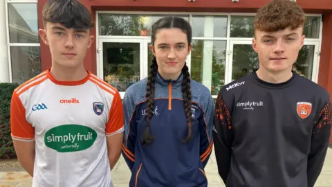 Three children standing next to each other outside wearing Armagh gear.