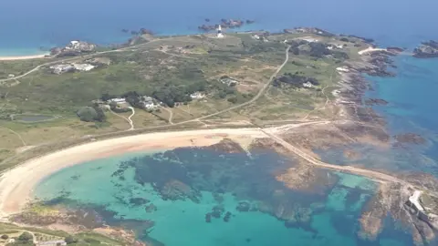 Aerial view of a coastal town with sandy beaches, rocky shoreline, turquoise bays, and patchwork fields stretching inland.