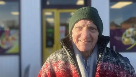 Photograph of 90 year-old Keith Brown from Derker in Oldham. He is pictured wearing a hat - standing outside a convenience store. 