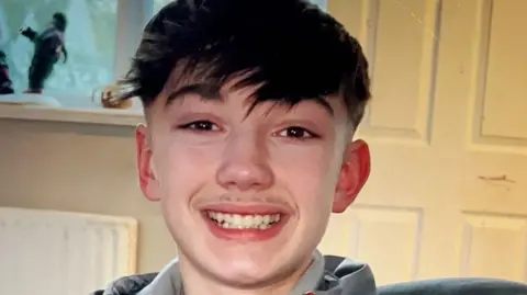 Christopher McBurnie, a teenager with short dark hair and a long fringe, smiling.