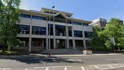 Google Kingston Crown Court - a grey, square building with trees on either side. There is a lamp post and a bike outside. 