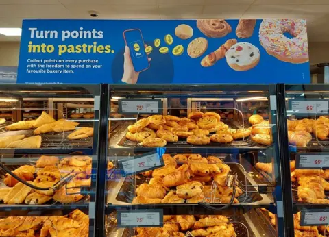 BBC The pastry section at Lidl, with a sign above it saying "turn points into pastries"