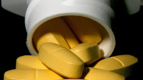 Yellow pills being poured out of a white medicine bottle.