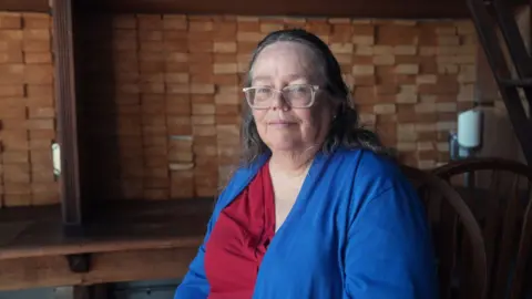 Gareth Fenley sits in a cafe wearing a blue cardigan over a red shirt