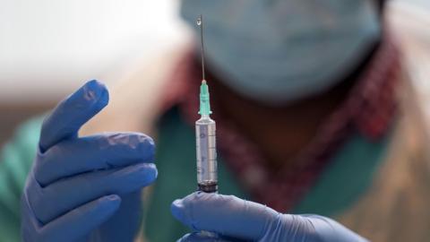 A vaccine, being held by an out of focus doctor