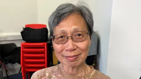 Hing Chan looking directly at the camera. She is sitting in a conference room at Chipping Barnet Library