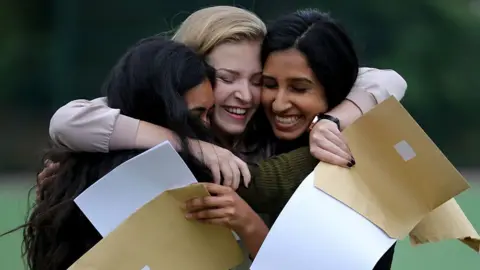 Getty Images Three teenage girls smiling and hugging, holding their GCSE results in their hands.