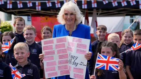 PA Media Queen Camilla poses with local school children holding a birthday card, during a visit to Les Cotils at L'Hyvreuse, in Saint Peter Port, Guernsey