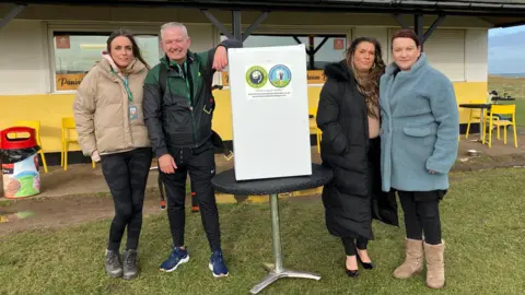 Tom Judge standing with Stacey Baldam and two other members of the team with the fridge in the middle.