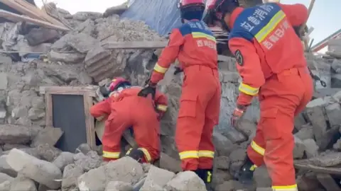 Rescue team dressed in red overalls search through rubble in Tibet 