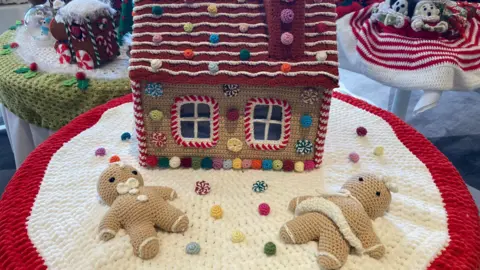 Katy Lewis/BBC A post box topper in red and white decorated with two gingerbread and a gingerbread house.