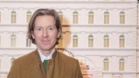 Wes Anderson posing in front of a model of the Grand Budapest Hotel, which is one of more than 600 objects that will be included in a Wes Anderson exhibition in London