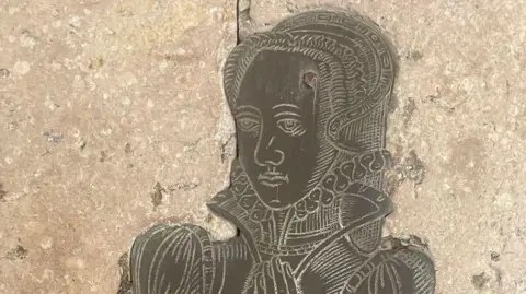 Dr Louise Ryland-Epton Part of an old brass engraving of a woman in a Tudor dress, attached to a stone wall.