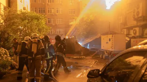 An explosion is seen after a Russian drone strikes a building as Ukrainian firefighters battle a fire in another building previously hit by a drone during a Russian air attack on Kyiv,