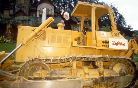 SIPA/Shutterstock Dolly Parton waves from a big yellow construction truck at the ground breaking ceremony for her Dollywood theme park, September 1985