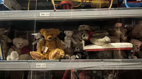 Shelf stuffed with lots of teddy bears of all different colours - mainly white and brown. 