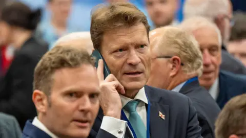 PA Media Richard Tice speaking on a phone while waiting for the result