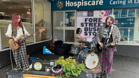 Three young members of a band playing the drums, guitar and singing on a street corner