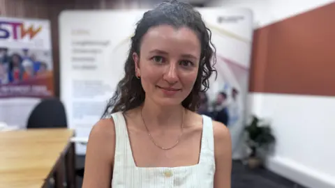 Picture of a woman in a white jumpsuit with long brown hair.