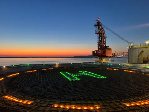Archie Clarke The sun sets in the distance, with the picture taken from an oil rig - a heli pad, lit up by electronic lights is where the picture was taken from.